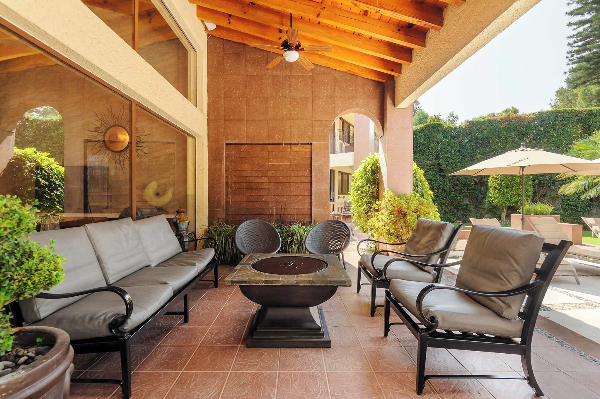 Un patio exterior con sofá, sillas, un brasero y plantas en macetas.