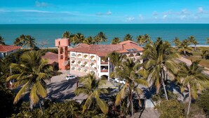Un hotel frente al mar con un edificio central que presenta balcones en arco, una torre de agua y un estacionamiento.