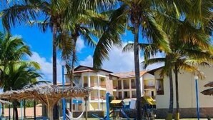 Una playa con palmeras, una hamaca y un edificio con balcones.