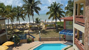 Zona de piscina con sillones de descanso, una piscina pequeña y vistas a la playa y el océano.