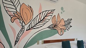 Habitación de hotel con cama, aire acondicionado de pared y un mural floral.
