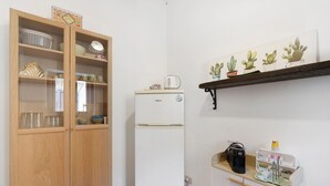 A compact kitchen with a refrigerator, wooden cabinet, and a shelf with potted plants. - Apartment 'Le Caravelle - Apt 2' (Castellammare del Golfo)