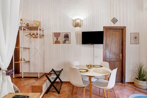 Een eetruimte met een ronde tafel, witte stoelen, een televisie en een schoenenrek.