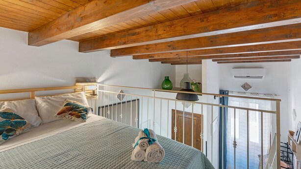A bedroom with a wooden ceiling, a bed with a rolled towel, a green vase, and a small table with a lamp. - Apartment 'Le Caravelle - Apt 36' (Castellammare del Golfo)