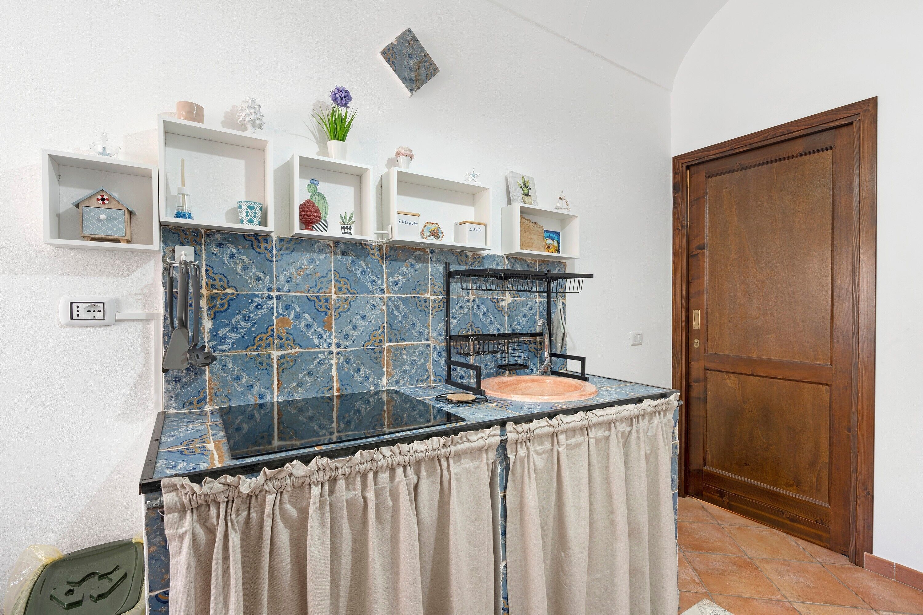 A kitchen with blue patterned tiles, a black countertop, and a wooden door.