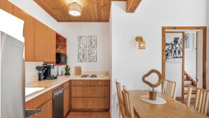 A kitchen with wooden cabinets, a dishwasher, and a dining area with a wooden table and chairs. - Fire Island Pines paradise (Fire Island)