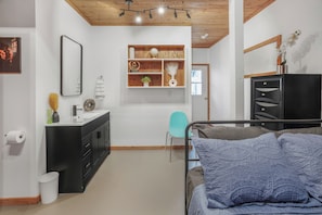 Une chambre à coucher comprenant un lit, une table de chevet, une commode, un miroir, une fenêtre et une étagère murale agrémentée d’objets décoratifs.