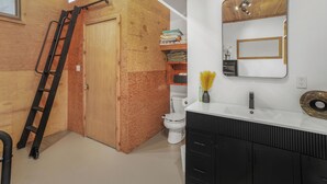 A bathroom with a wooden door, a white toilet, a black vanity with a mirror, and a white sink. - Fire Island Pines paradise (Fire Island)