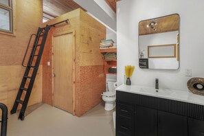 A bathroom with a wooden door, a white toilet, a black vanity with a mirror, and a white sink.