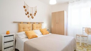 Een slaapkamer met een bed, een kledingkast, een nachtkastje, een macramé decoratie en een stoel.