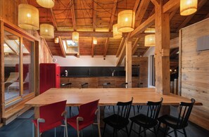 Un grand espace dédié à la salle à manger, avec une longue table en bois et des chaises, un réfrigérateur rouge et une cuisine en arrière-plan.