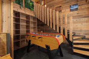 A wooden-floored room with a foosball table, shelves, and a staircase. - Stone Lodge - 8 pers - Sauna - Bain nordique (Gérardmer)