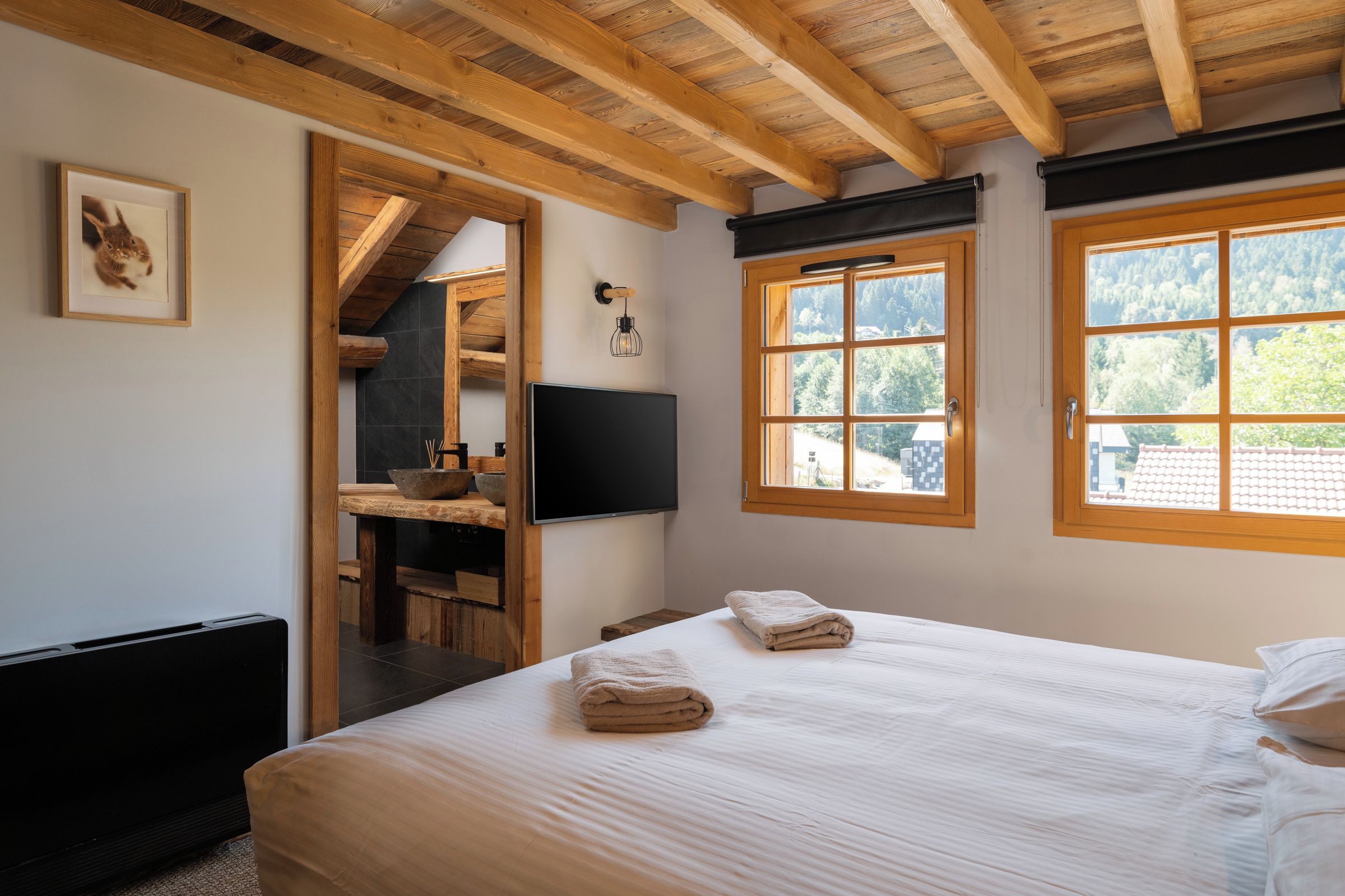 A bedroom with a bed, a wooden desk, a television, and a window with a view of trees.