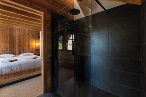 A modern room with a wooden ceiling, a bed with white bedding, a dark tiled wall, and a shower area. - Stone Lodge - 8 pers - Sauna - Bain nordique (Gérardmer)