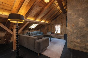 A cozy attic room with a wooden ceiling, a sofa, a lamp, and a stone wall. - Stone Lodge - 8 pers - Sauna - Bain nordique (Gérardmer)