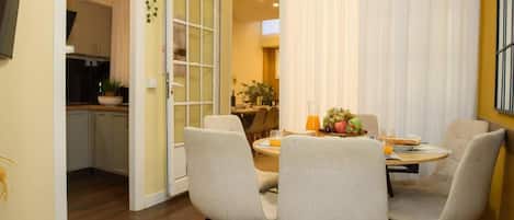 A dining area with a table set for four, chairs, a fruit bowl, and a view into the kitchen.