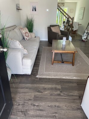Ein Wohnzimmer mit einer Couch, einem Couchtisch, einem Teppich und einer Treppe, die in einen anderen Raum führt.