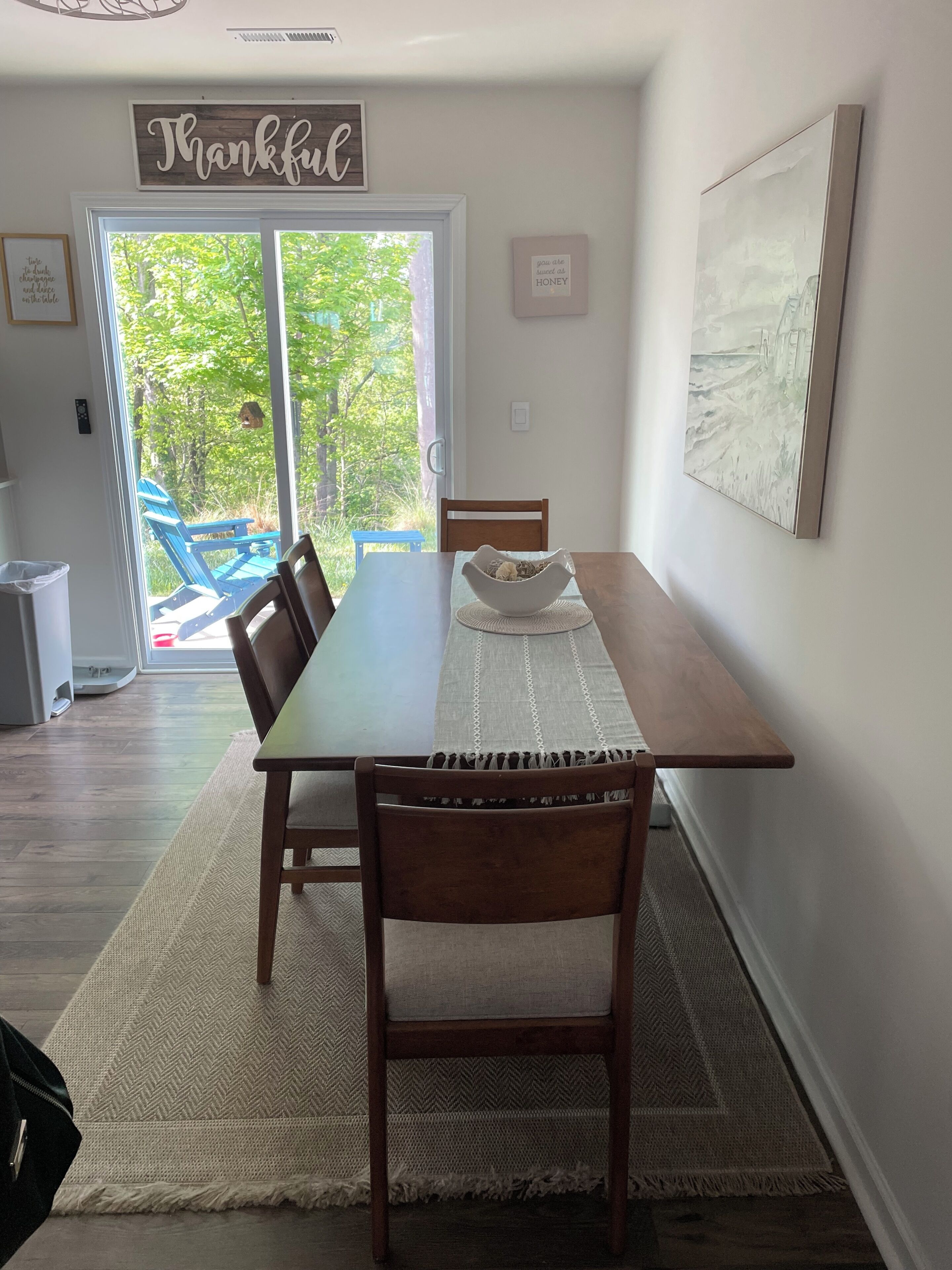 Un área de comedor con una mesa, sillas, un tapete, un letrero y un cuadro.