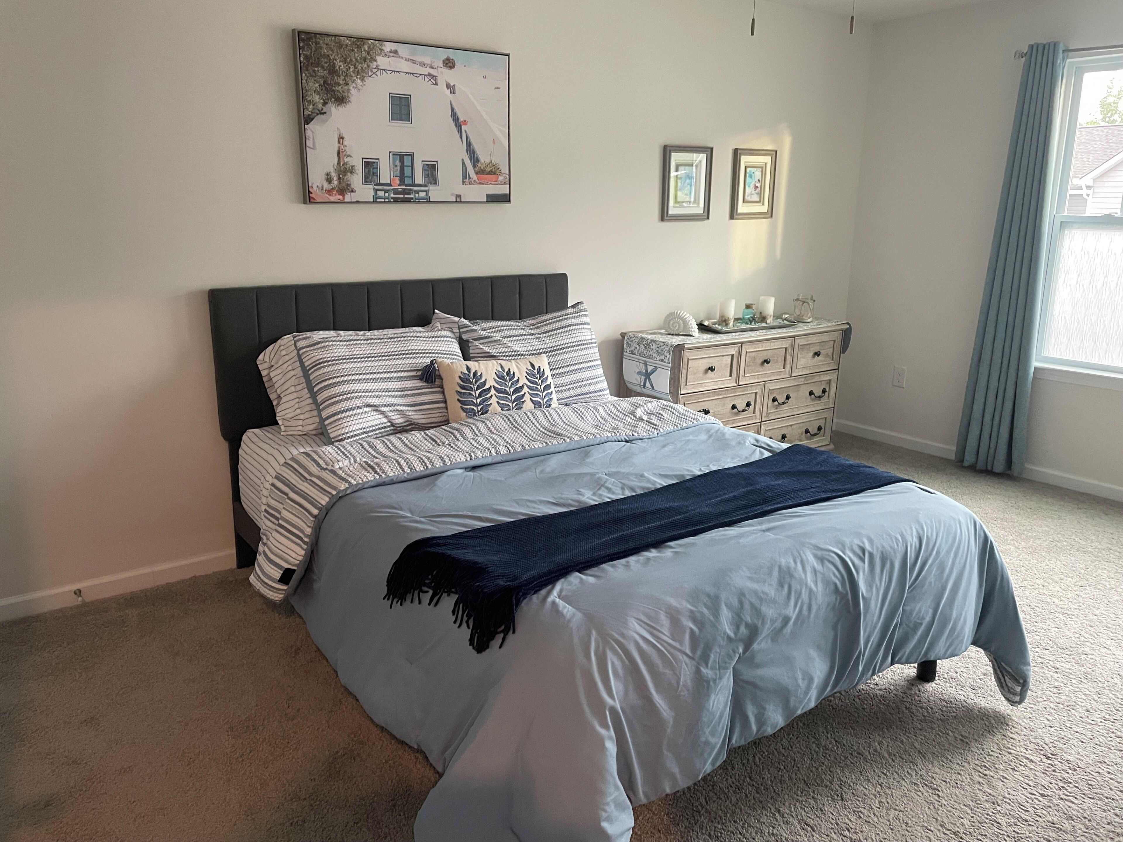 A bedroom with a bed, a dresser, a nightstand, and a painting on the wall.