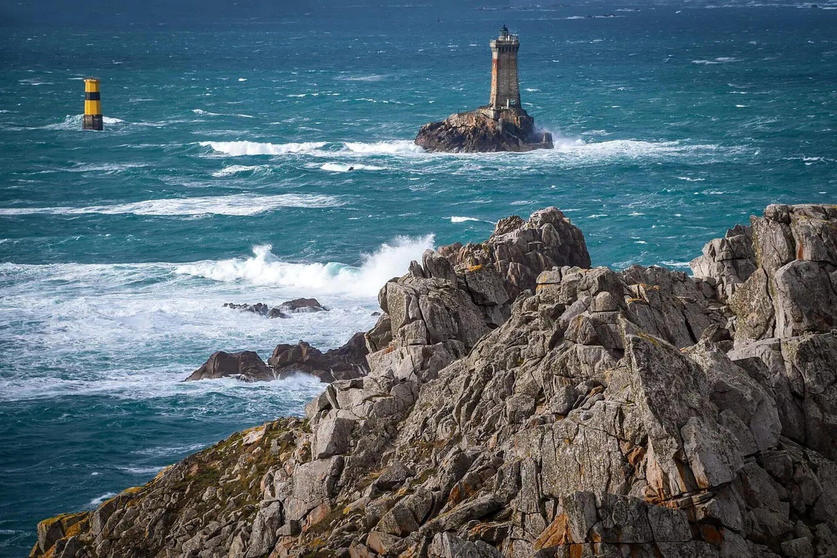 A rocky coastline with a lighthouse and a buoy in the sea.