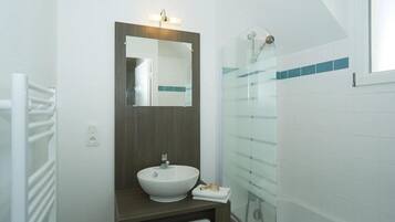 A modern bathroom with a white sink, a mirror, and a glass shower enclosure.