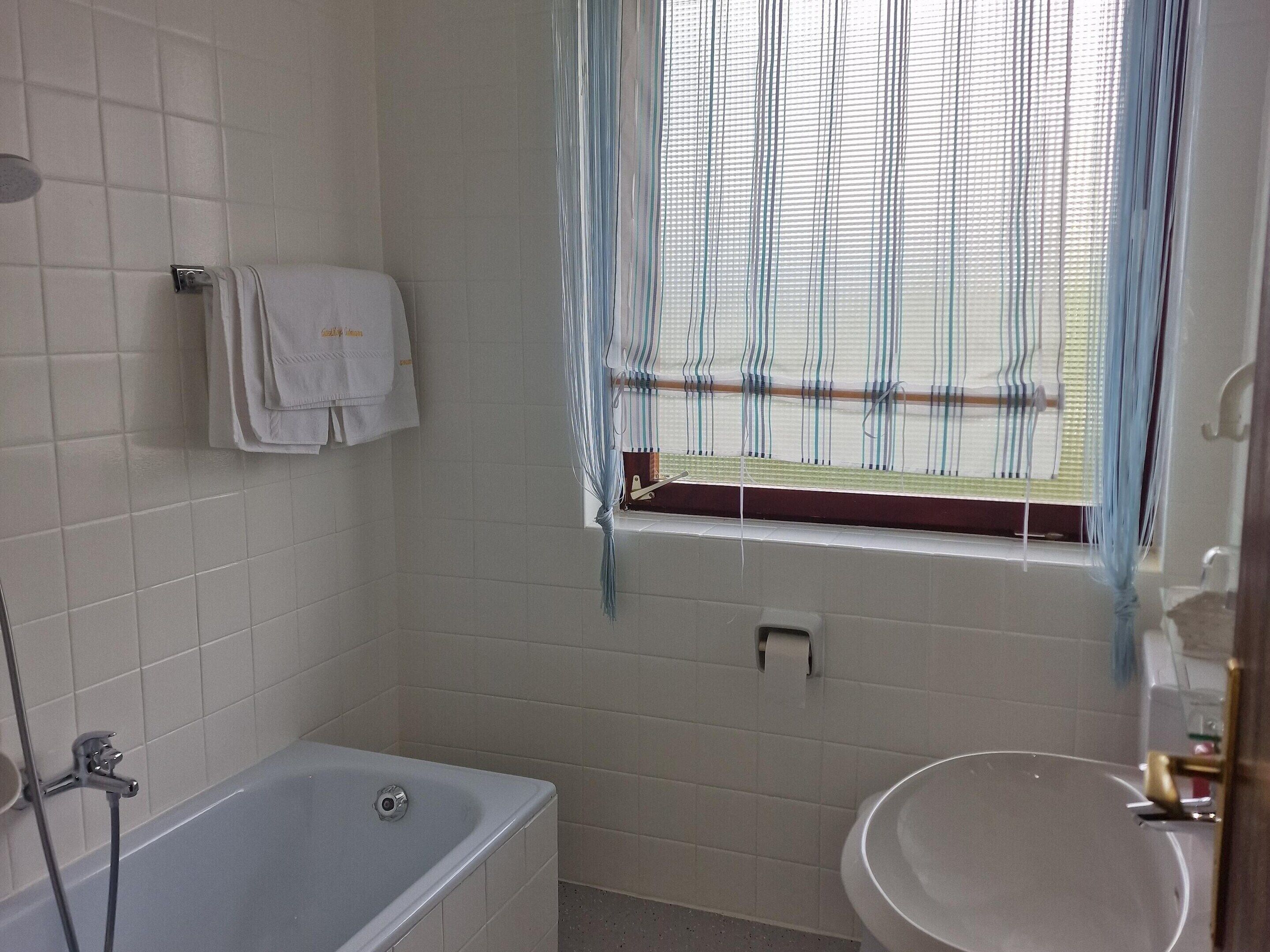 A bathroom with a bathtub, a sink, and a window with a curtain.