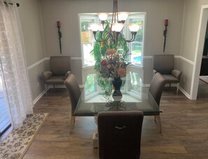 A dining area with a glass table, cushioned chairs, a chandelier, and a vase with flowers. - Relax, Swim & Unwind at Bella Casa's Private Pool Retreat Sleeps 6 Pet friendly (Valdosta)
