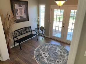 Un foyer avec un banc, un tapis, une porte dotée de panneaux de verre et un luminaire fixé au mur.