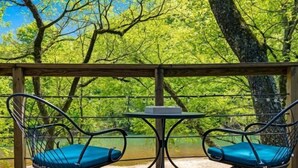 Um deck com duas cadeiras e uma mesa, com vista para a água e árvores.