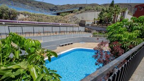 Piscina cercada por vegetação, com grade ao redor e vista distante de uma linha de trem.