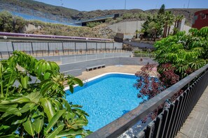 Une piscine entourée d’une clôture, agrémentée de verdure, et offrant une vue lointaine sur une voie ferrée.