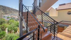 Uma escadaria com guarda-corpos de metal leva a uma varanda com vista para uma área residencial, com casas e uma colina ao fundo.
