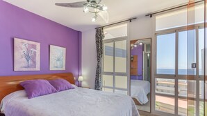 Quarto com cama, ventilador de teto, janela com vista e porta para área externa.