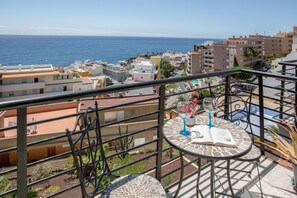 Un balcon avec vue sur la mer, une table carrelée et une plante en pot.