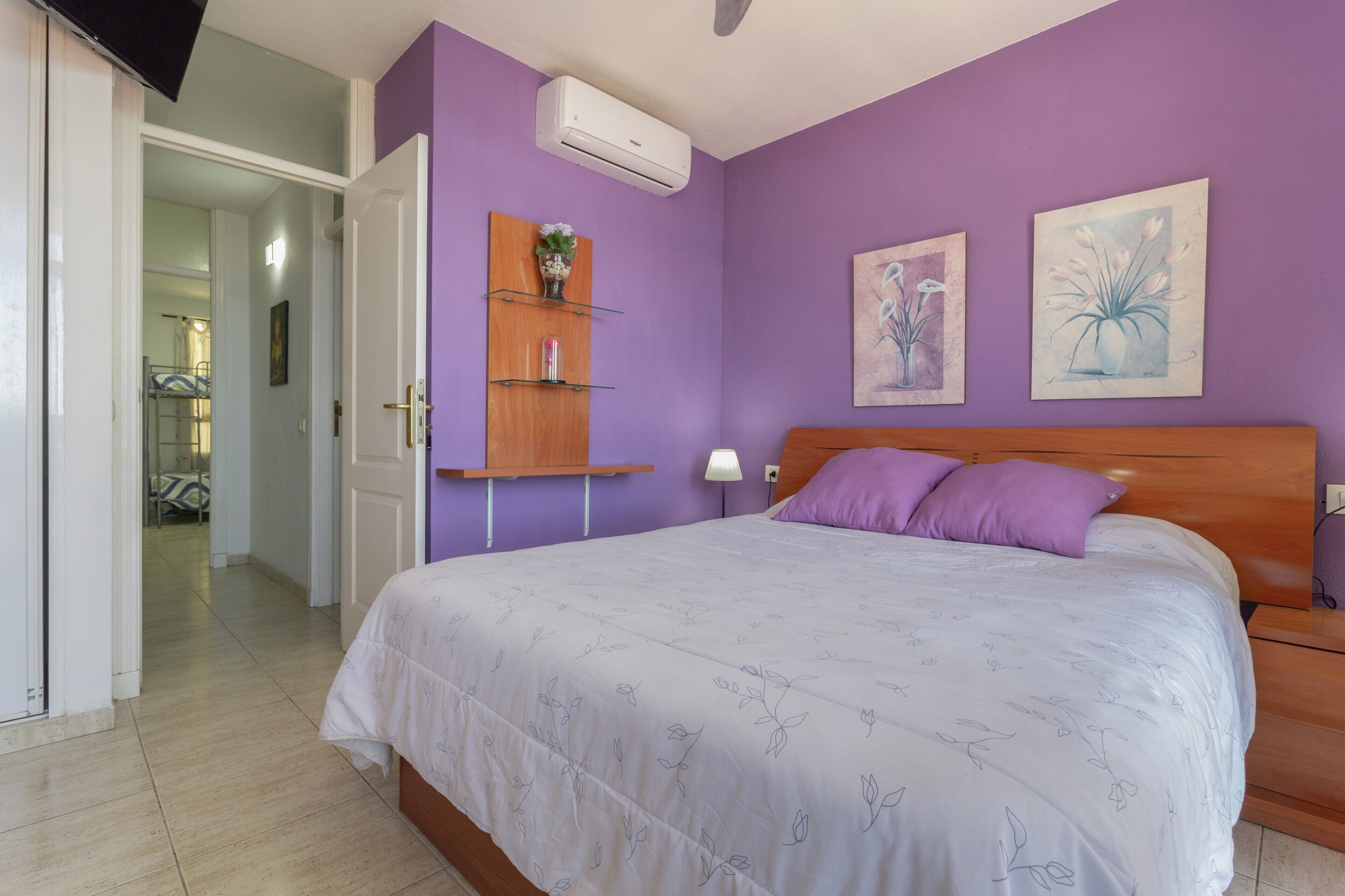 Un dormitorio con cama, cabecera de madera, estante con un florero y dos cuadros en la pared.