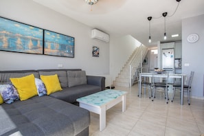 Un salon avec un canapé gris, des coussins jaunes, une table basse blanche et un escalier menant à un espace cuisine.