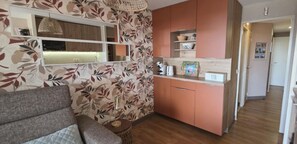 Ein kompakter Wohnbereich mit Sofa, Küchenzeile mit Schränken, einer Pendelleuchte und Holzboden.