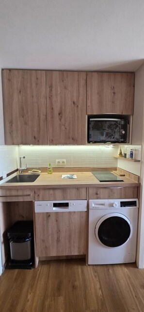 Eine kompakte Küche mit Holzausstattung, einer Mikrowelle, einem Geschirrspüler und einer Waschmaschine.