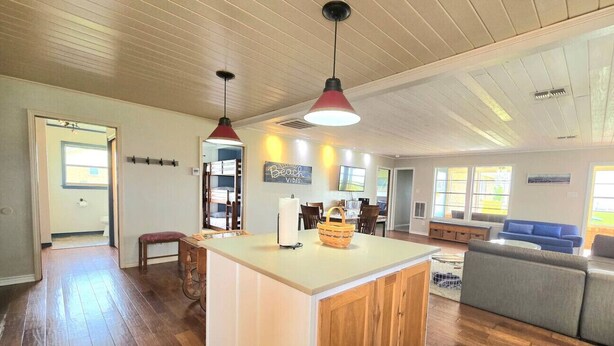 A spacious living area with a wooden floor, a central island with a sink, a blue sofa, and pendant lighting. - Waterfront, Lighted Pier and Family Games! (Port Lavaca)