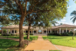 A building with a covered walkway, surrounded by greenery and palm trees.