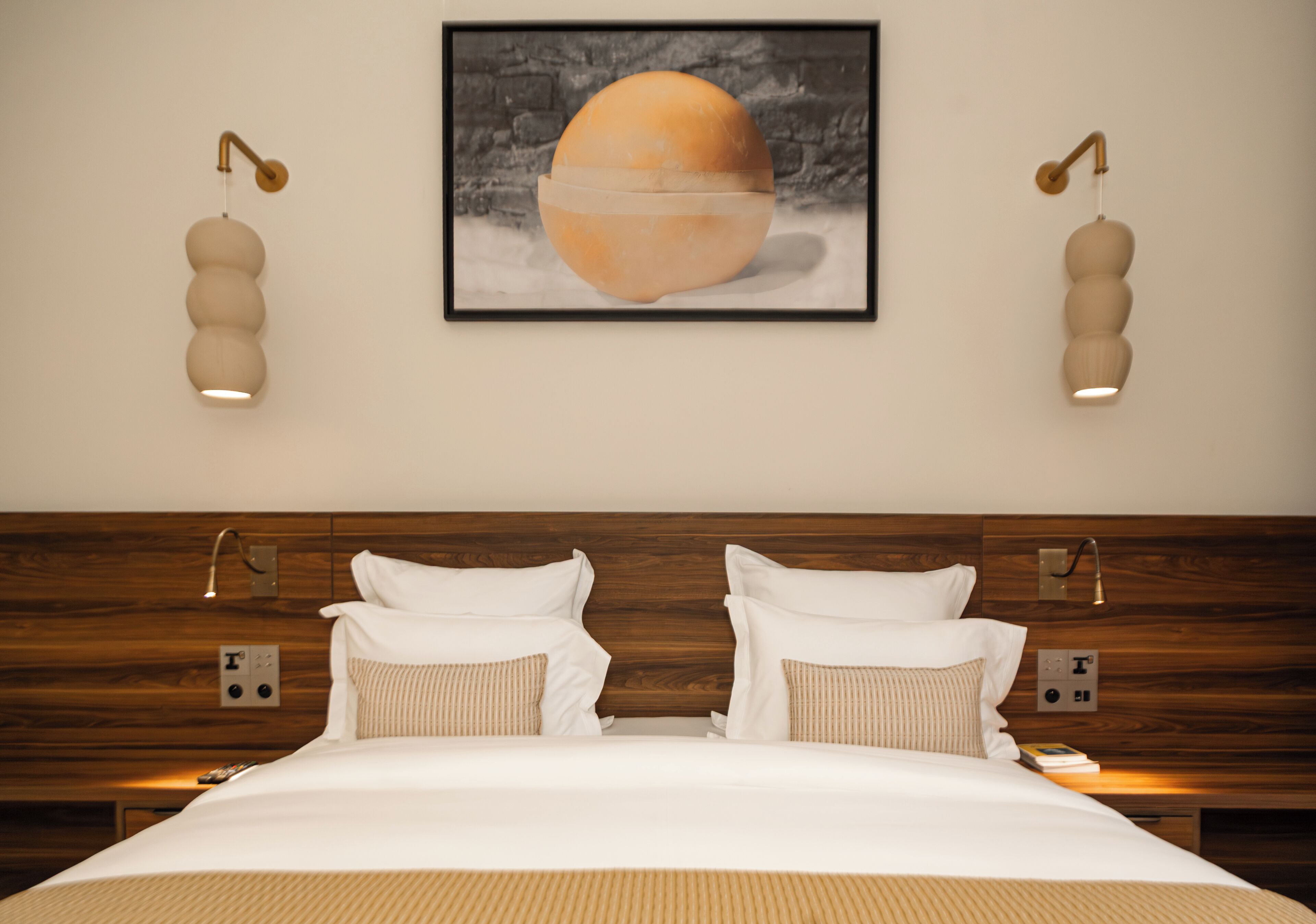 Habitación de hotel con cabecera de madera, una cama grande con ropa blanca, dos mesitas de noche y un cuadro en la pared.