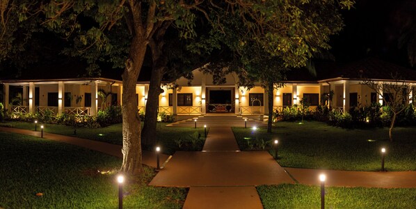 Un hôtel avec un chemin central menant à un bâtiment, entouré d’arbres et éclairé par des lampadaires.