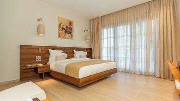 A modern hotel room with a large bed, wooden headboard, bedside tables, a desk, and a window with curtains.