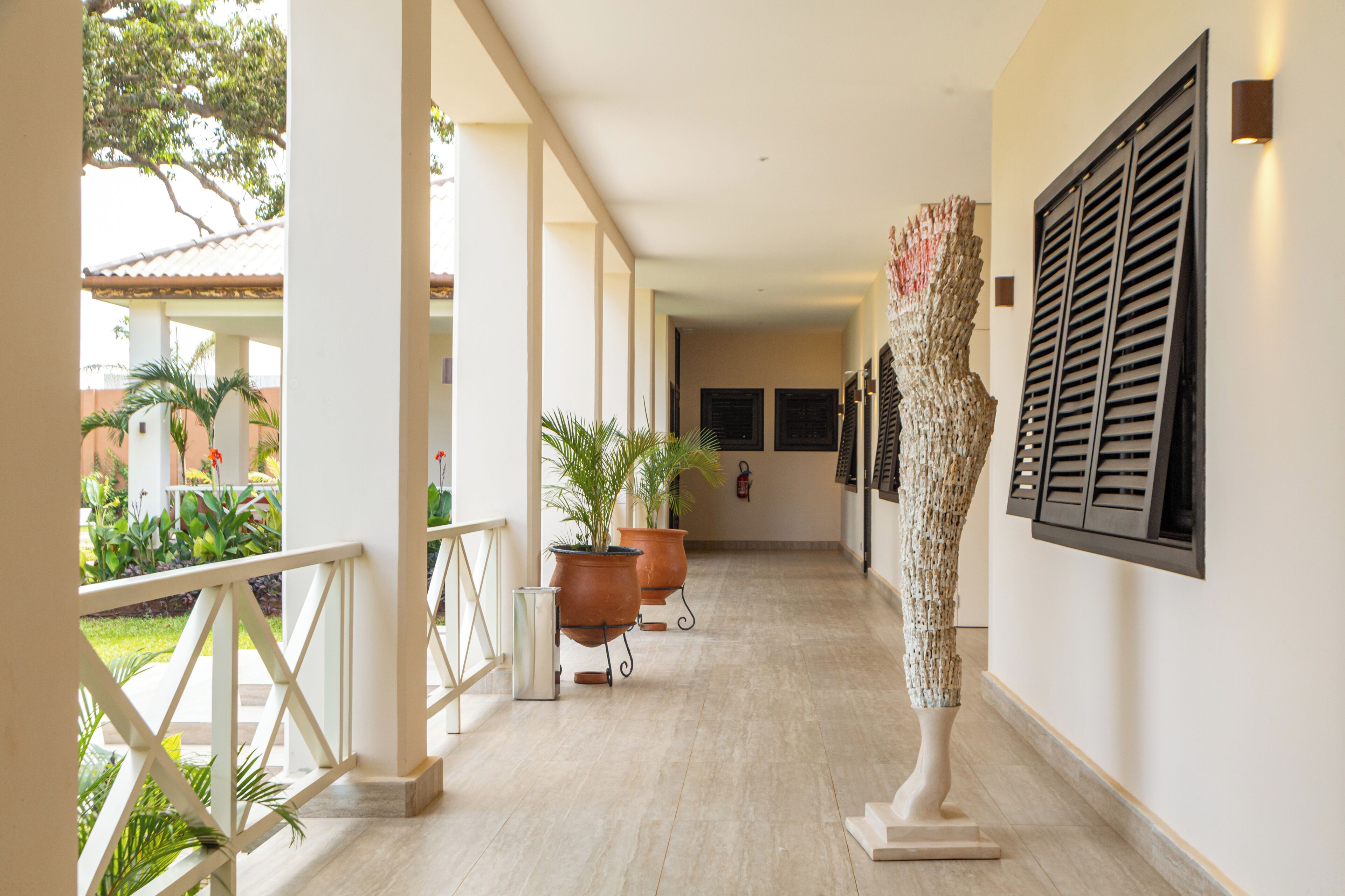 Un pasillo con barandilla blanca, plantas en macetas, una escultura e iluminación empotrada en la pared.