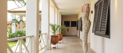 Un pasillo con barandilla blanca, plantas en macetas, una escultura e iluminación empotrada en la pared.