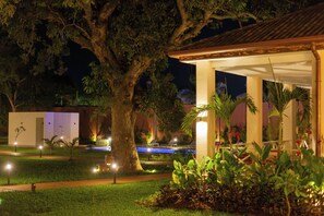 A nighttime view of a hotel with a large tree, a covered outdoor area, and a pool. - Native Hotels (Ouidah)