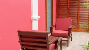 Un conjunto de banco y silla de madera frente a una pared rosa, con una puerta de madera y una planta de bambú al fondo.