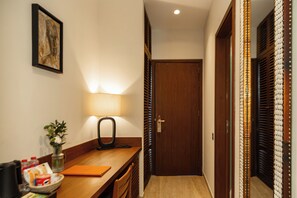 A hotel reception area with a desk, a lamp, a framed artwork, and a door leading to another room.