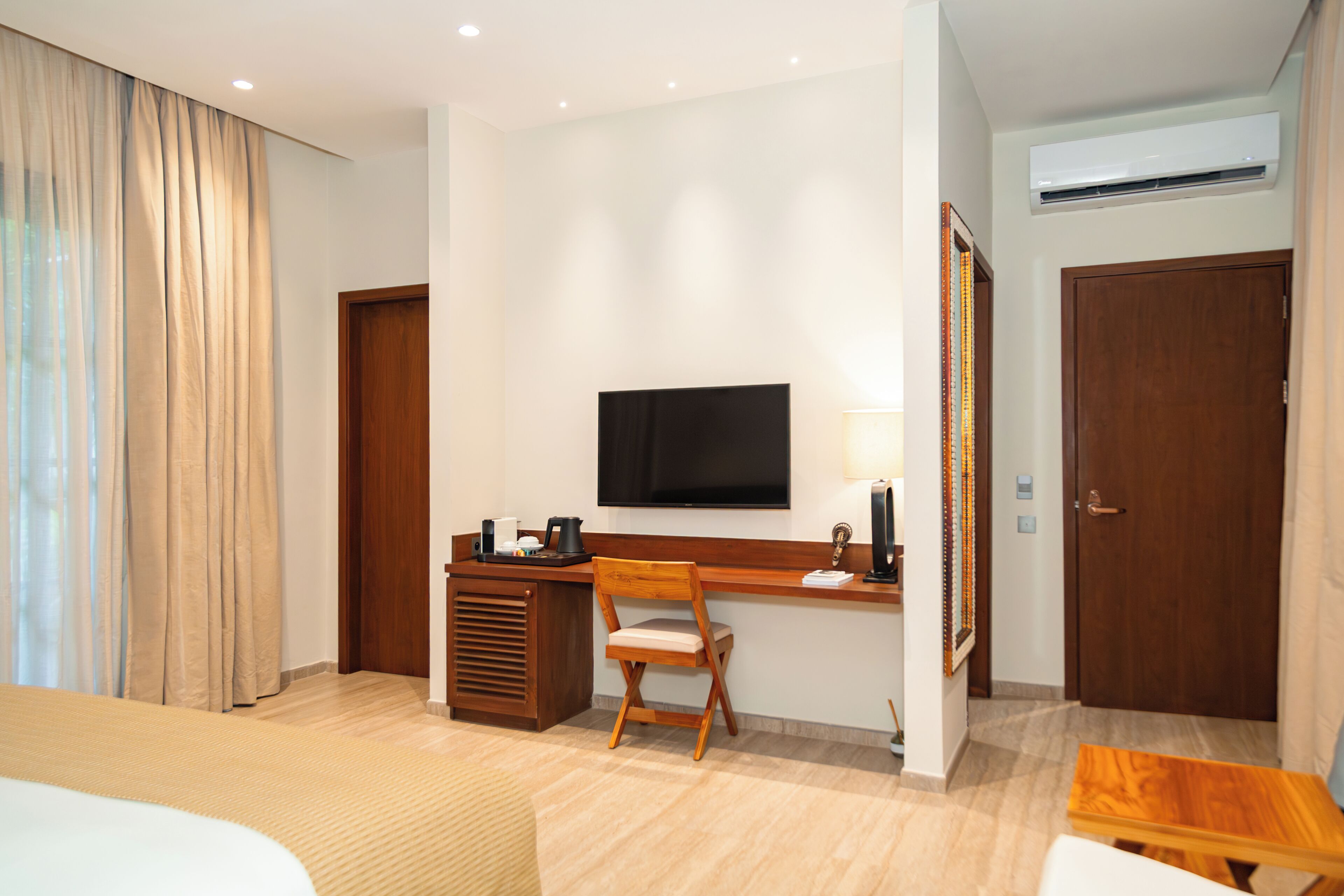 Quarto de hotel com cama, escrivaninha com cadeira, televisão e ar condicionado.