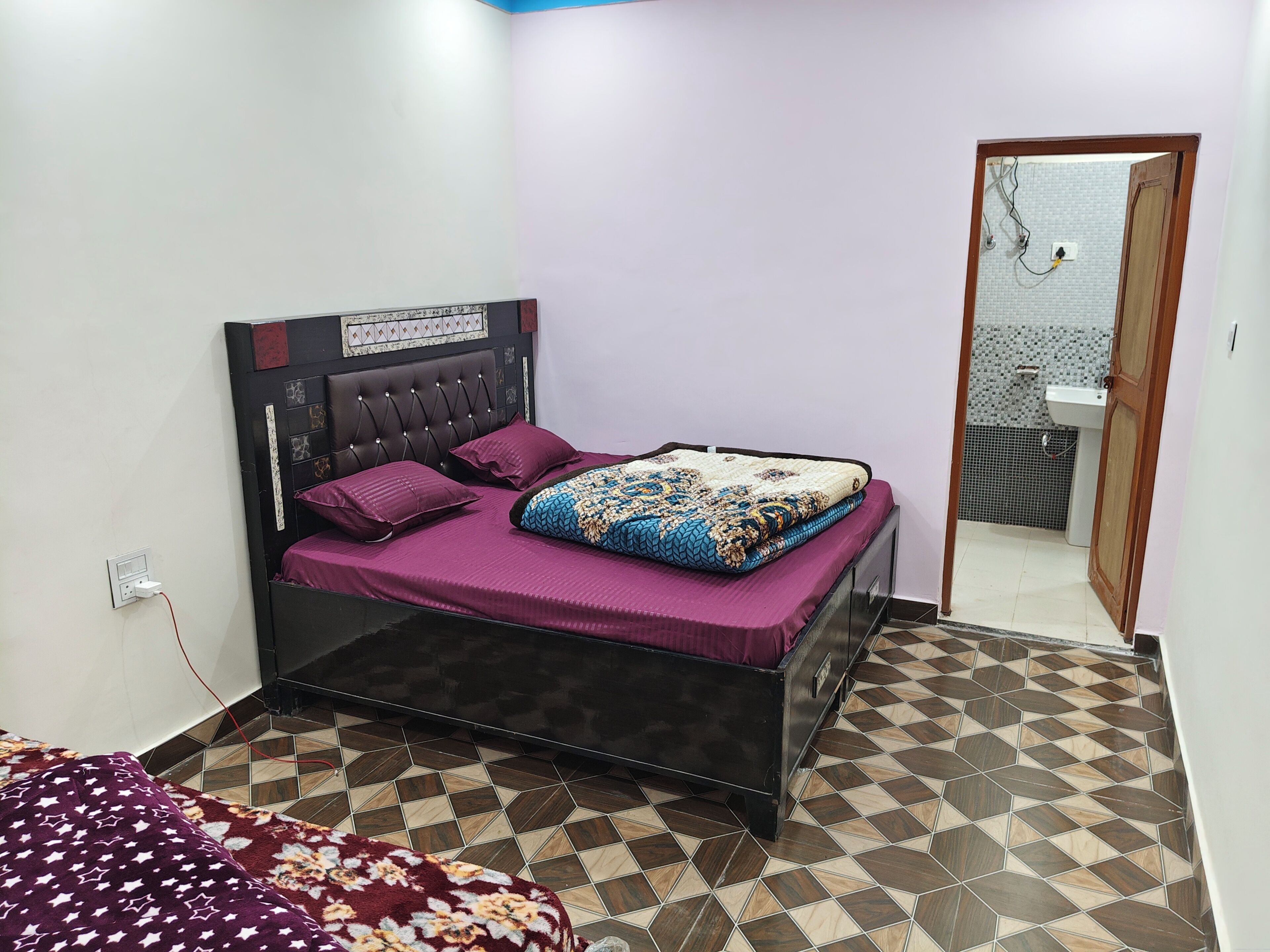 A bedroom with a bed, a nightstand, a wall socket, and a bathroom visible through an open door.